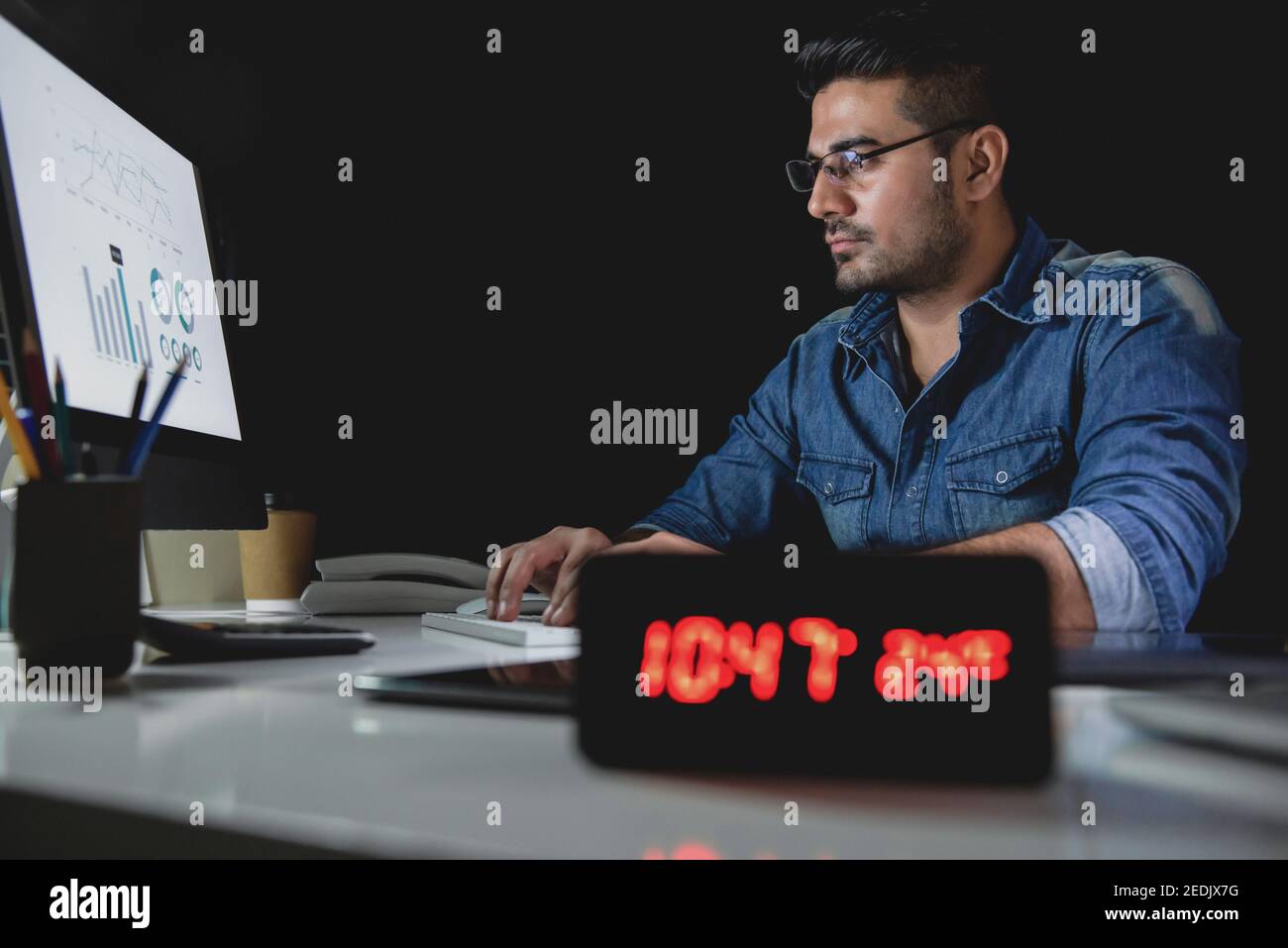 Workaholic asiatischen Mann bleiben Überstunden spät in der Nacht in die Büro, das sich auf die Arbeit mit dem Computer an seinem Schreibtisch konzentriert Stockfoto