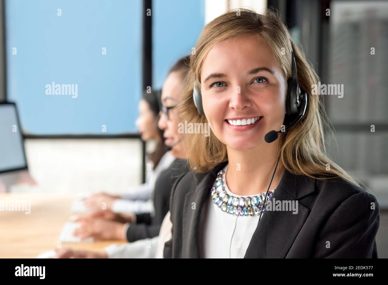 Freundliche, schöne kaukasische Frau, Telemarketing-Kundendienstmitarbeiter, der in arbeitet Call Center mit ihrem Team Stockfoto