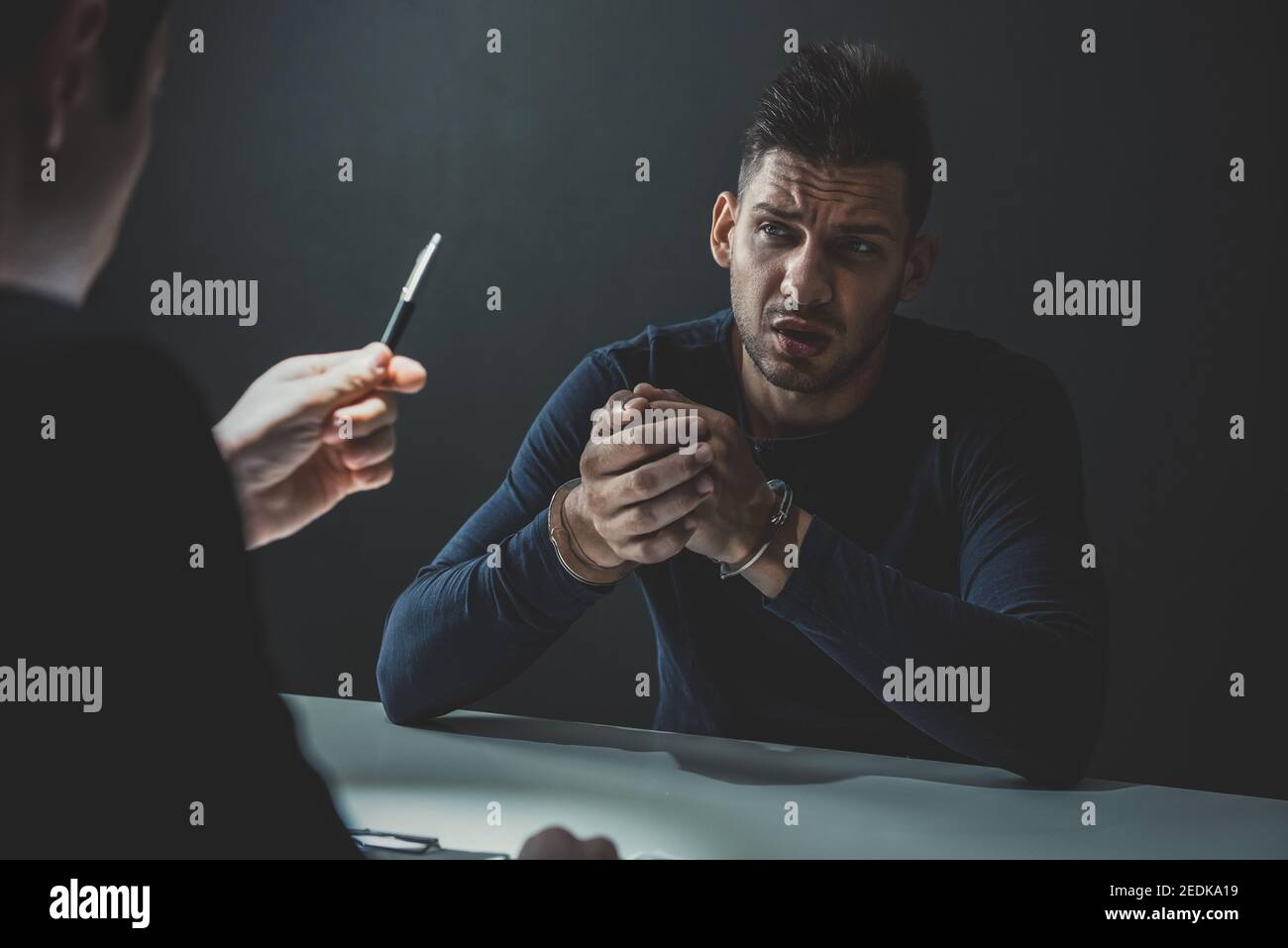Verdächtiger oder krimineller Mann mit Handschellen, der vom Detektiv interviewt wird Im Verhörraum Stockfoto