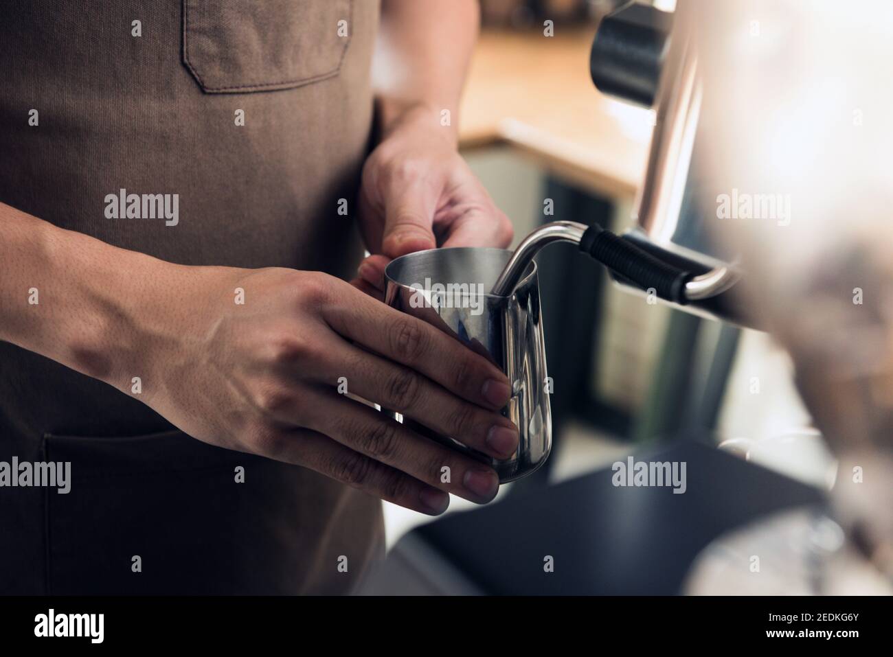 Barista dämpft Milch im Krug mit Kaffeemaschine Um Latte Kunst im Café zu machen Stockfoto
