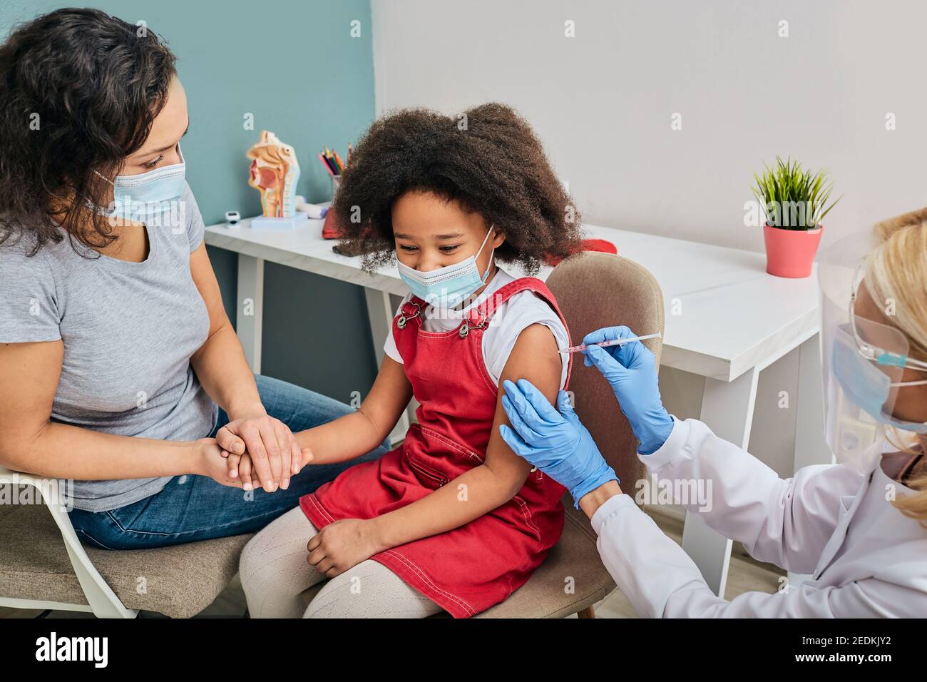 Routineimpfungen für ein Kind. Afroamerikanisches Mädchen und ihre Mutter tragen medizinische Masken, während sie von einem Hausarzt geimpft wurden Stockfoto