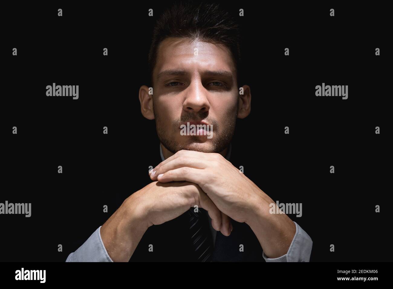 Nachdenkender Mann im schwarzen Anzug mit Händen am Kinn Dunkler Schatten starrt auf die Kamera Stockfoto