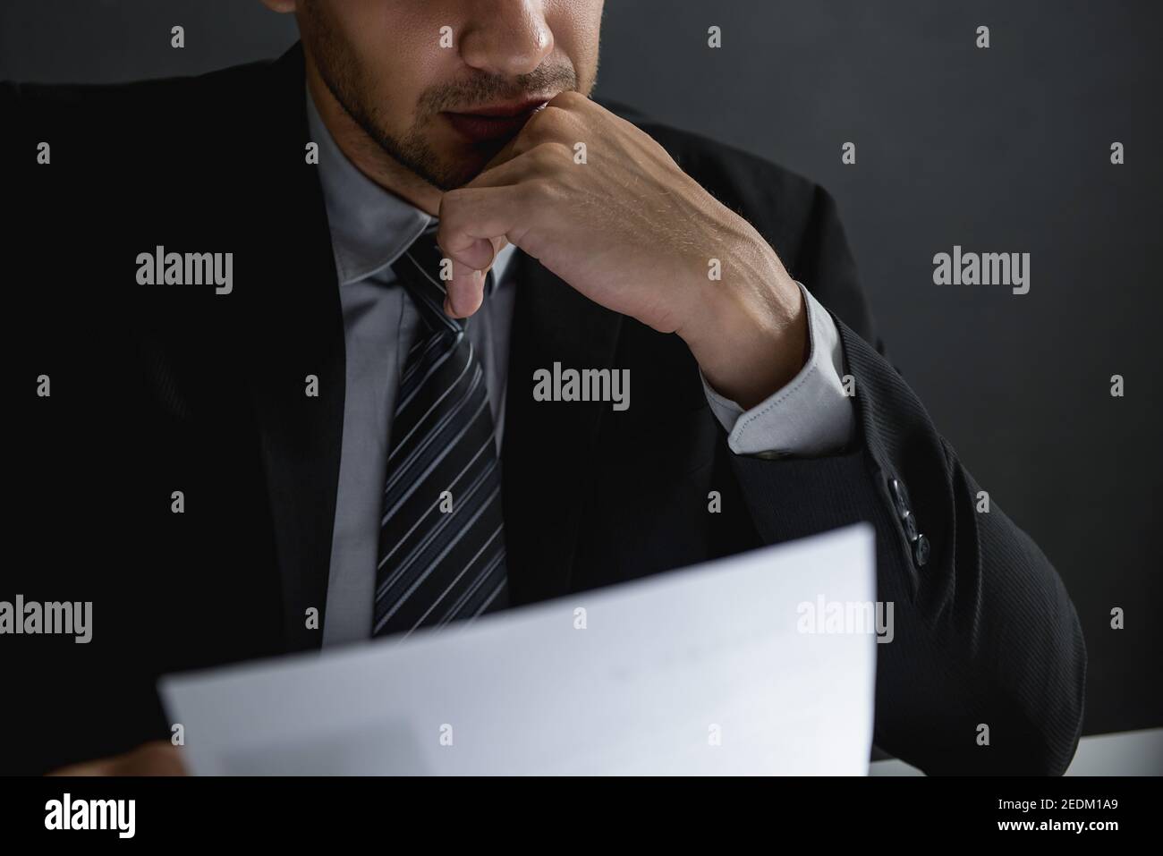 Serious Geschäftsmann mit Hand auf Kinn Lesen Dokument und Nachdenken Nachts im dunklen Zimmer Stockfoto