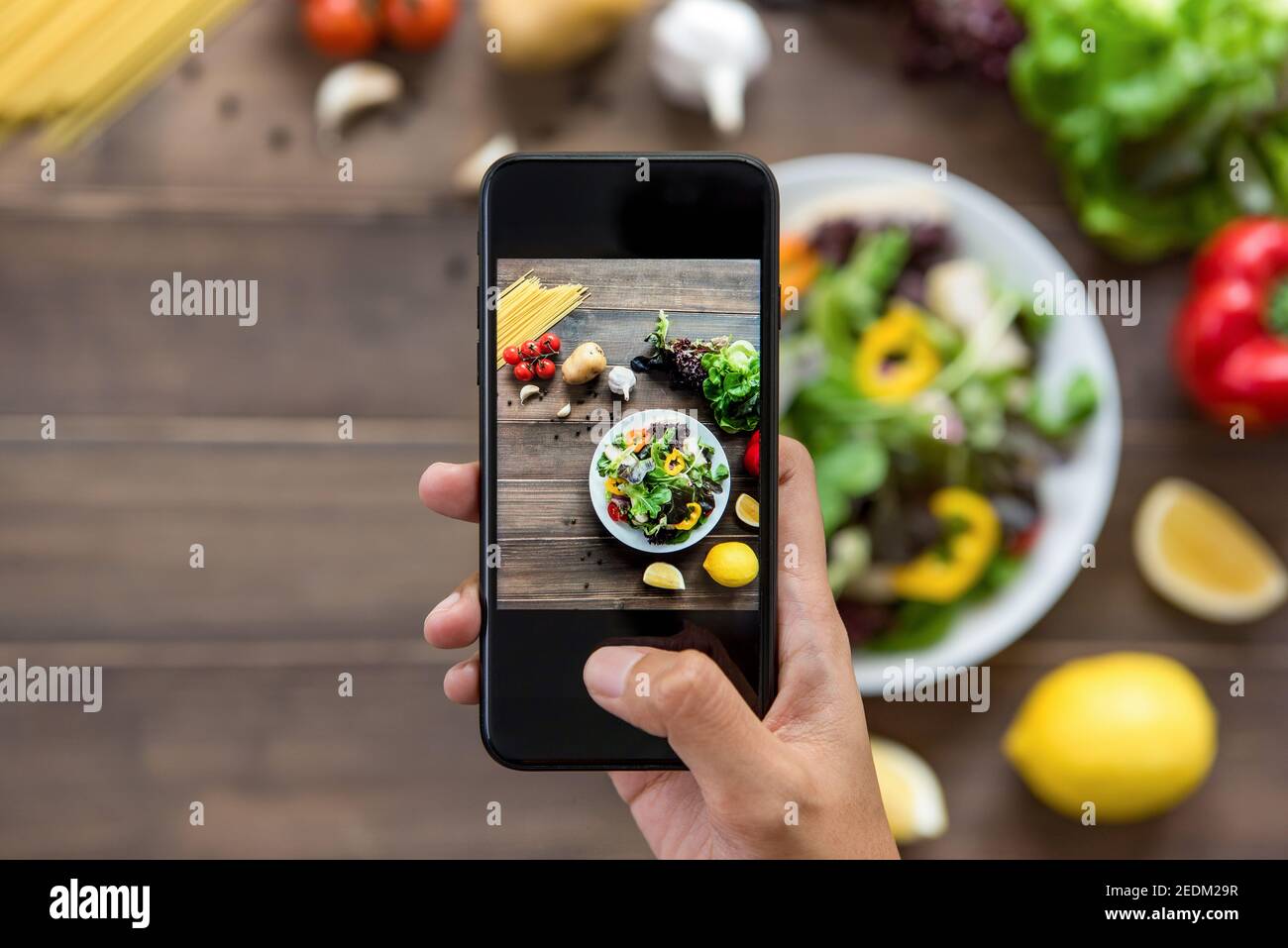 Food-Blogger mit Smartphone Foto von schönen Salat, rohe Spaghetti und Zutaten auf Holztisch zu teilen in den sozialen Medien Stockfoto
