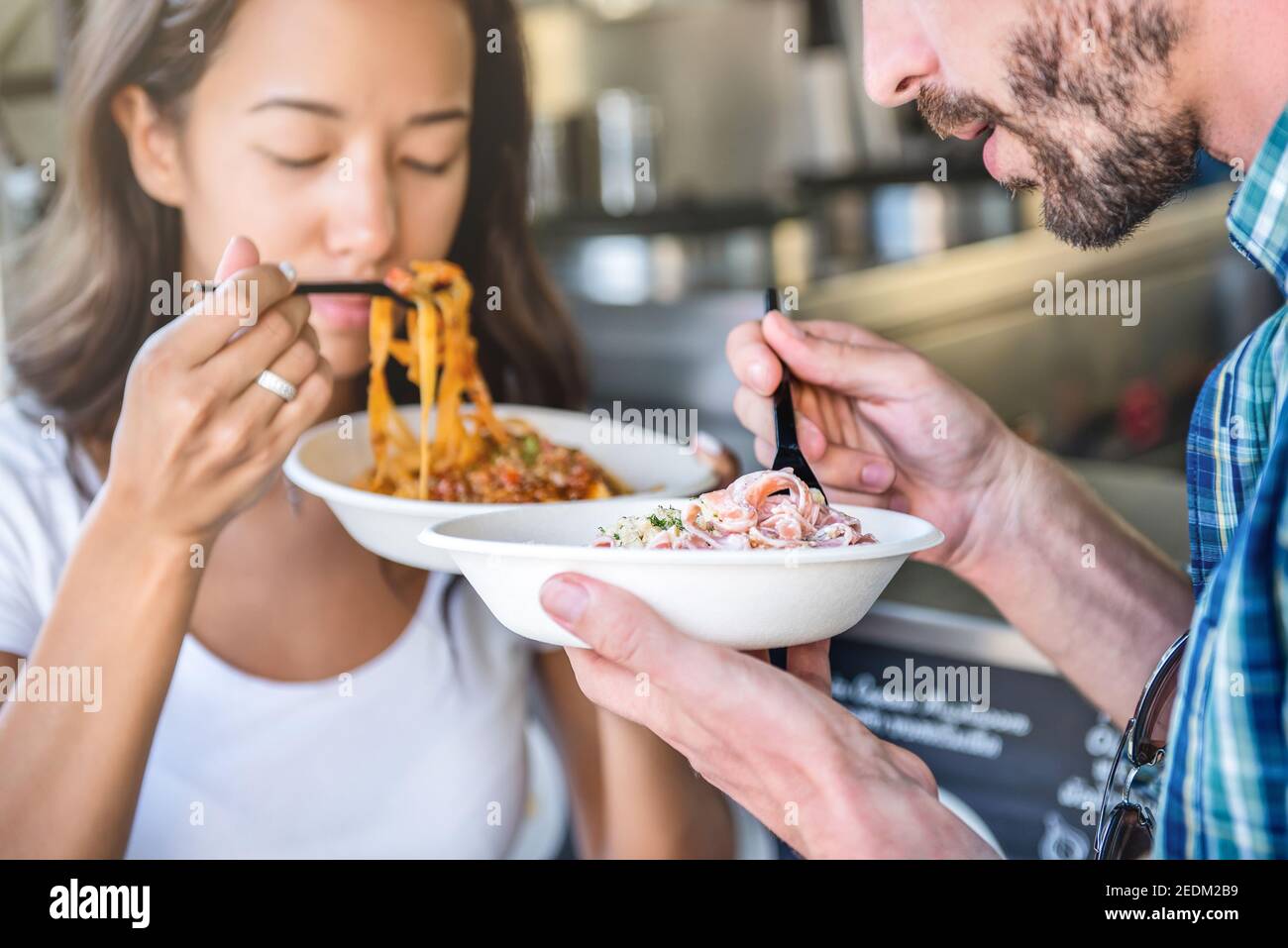Paar hält Teller mit Nudeln zum Mitnehmen am Food-Truck, essen mit Vergnügen Stockfoto
