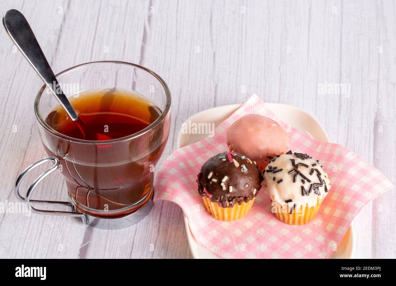 Cupcakes in verschiedenen Geschmacksrichtungen und Farben, begleitet von einer Tasse Tee Stockfoto