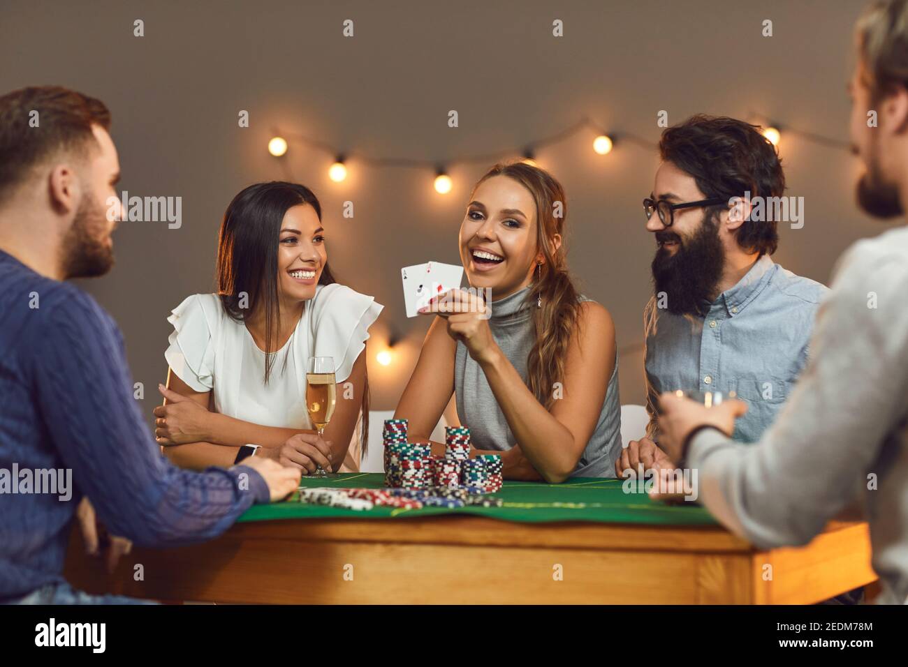 Glückliche junge Frau zeigt zwei Asse, während sie Poker mit ihren Freunden spielt. Stockfoto