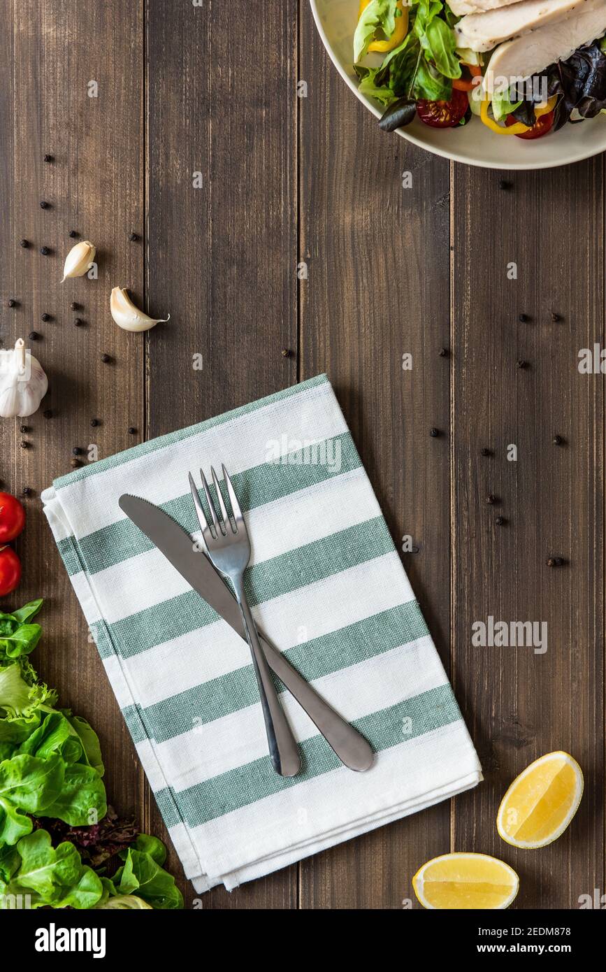 Gabel und Messer mit gesunden Zutaten und Hühnersalat auf Holztisch, Draufsicht Stockfoto