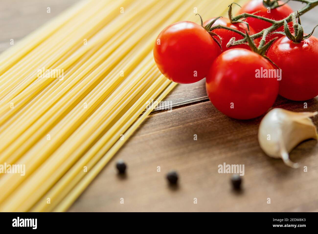 Zutaten, rohe Spaghetti mit roten Tomaten, Knoblauch und Pfeffer auf Holztisch zum Kochen vorbereitet Stockfoto