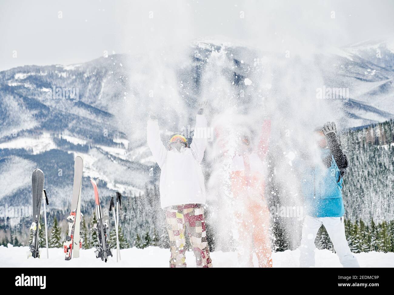 Drei Skifahrer in Skianzügen werfen frischen Pulverschnee hoch in die Luft, Spaß im Skigebiet mit schönen Bergen im Hintergrund. Konzept der Wintersport-Aktivitäten, Spaß und Beziehungen. Stockfoto