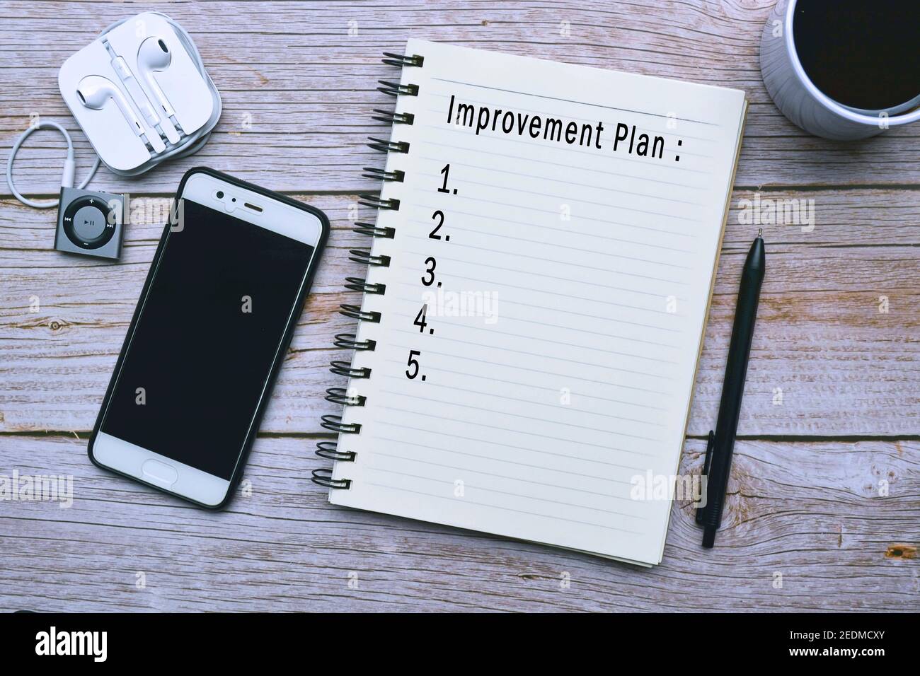 Text auf Notizblock mit Tasse Kaffee, Smartphone, Musik-Player und Stift auf Holzschreibtisch - Verbesserungsplan Stockfoto