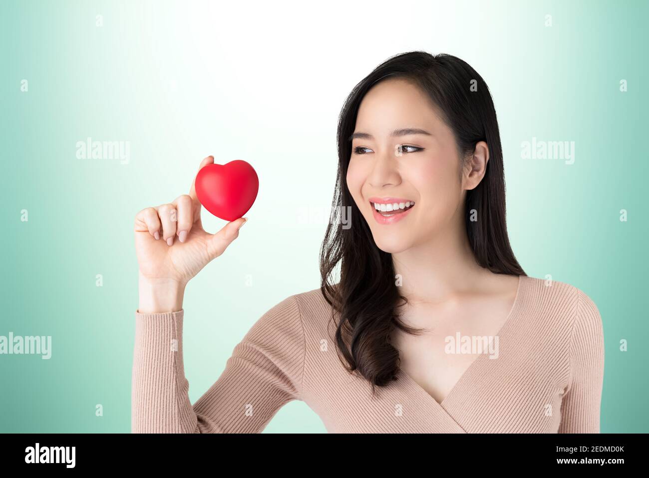Schöne gesunde junge asiatische Frau halten und Blick auf rot Herzball auf türkisgrünem Hintergrund Stockfoto