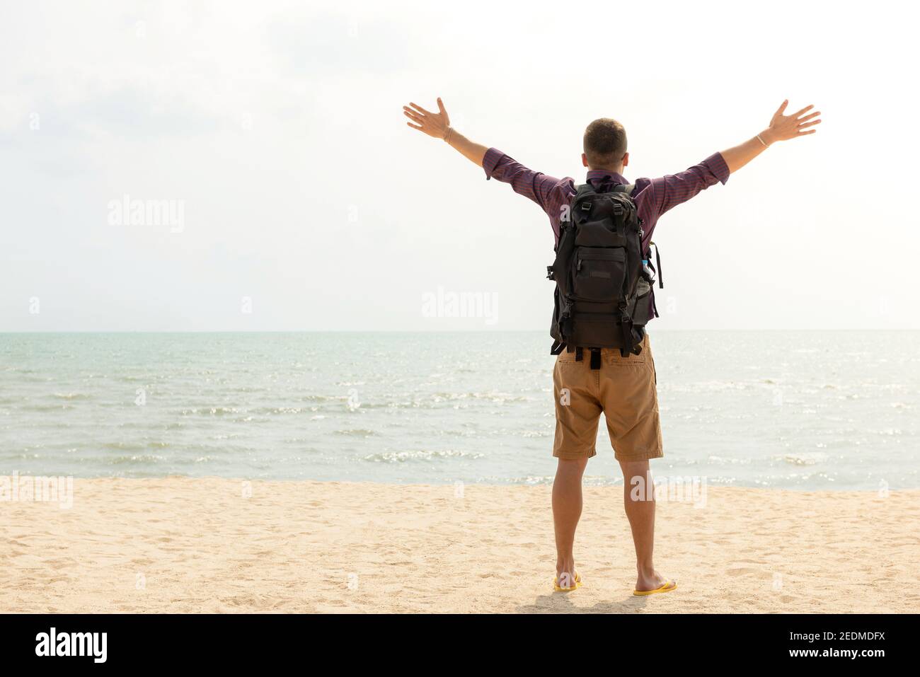 Happy Tourist Backpacker mit offenen Armen am Strand in den Sommerferien, Rückansicht mit Kopierraum Stockfoto