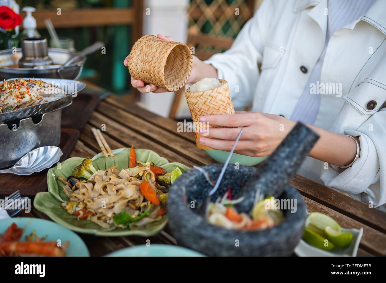 Frau öffnen klebrigen Reis Bambus-Behälter, während mit einem drei GusMenü in einem thailändischen Restaurant in der Nähe Stockfoto