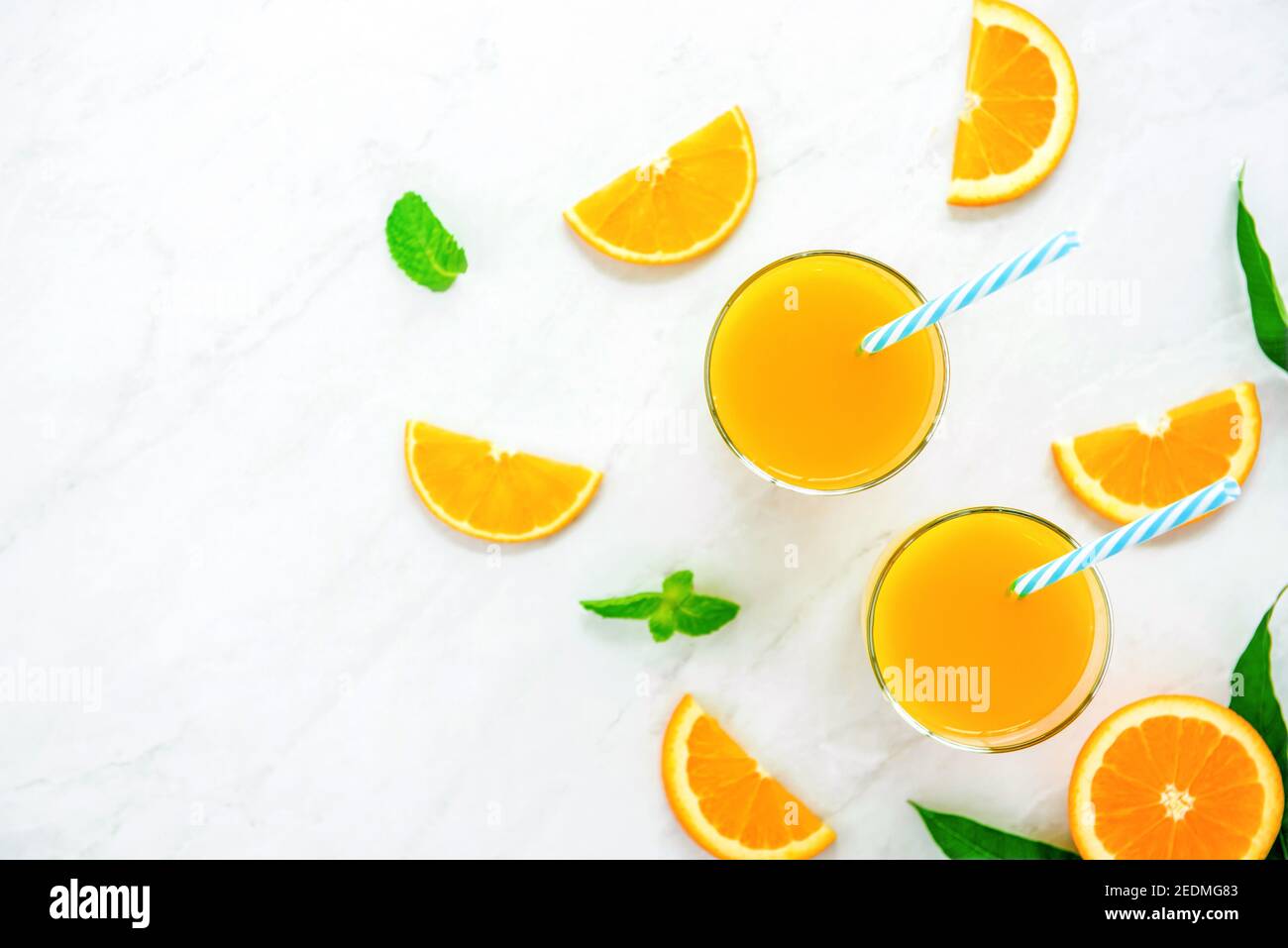 Erfrischende Getränke für den Sommer, kalter süßer und saurer tropischer Orangensaft mit Eiswürfeln in den Gläsern auf der Arbeitsplatte aus weißem Marmor, Blick von oben Stockfoto