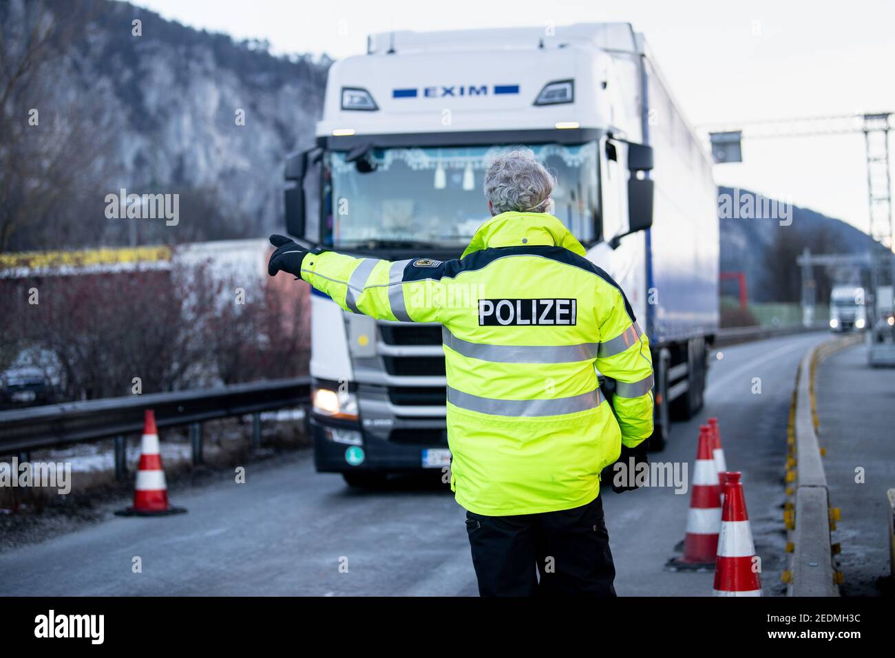 Kiefersfelden, Deutschland. Februar 2021, 15th. Ein Bundespolizist weist einen LKW-Fahrer aus Österreich in den Kontrollpunkt auf der Autobahn A93 bei Kiefersfelden. Die verschärften deutschen Einreisebestimmungen an der Grenze zum österreichischen Bundesland Tirol zum Schutz vor gefährlichen Varianten des Coronavirus sind am Sonntagabend in Kraft getreten. Quelle: Matthias Balk/dpa/Alamy Live News Stockfoto