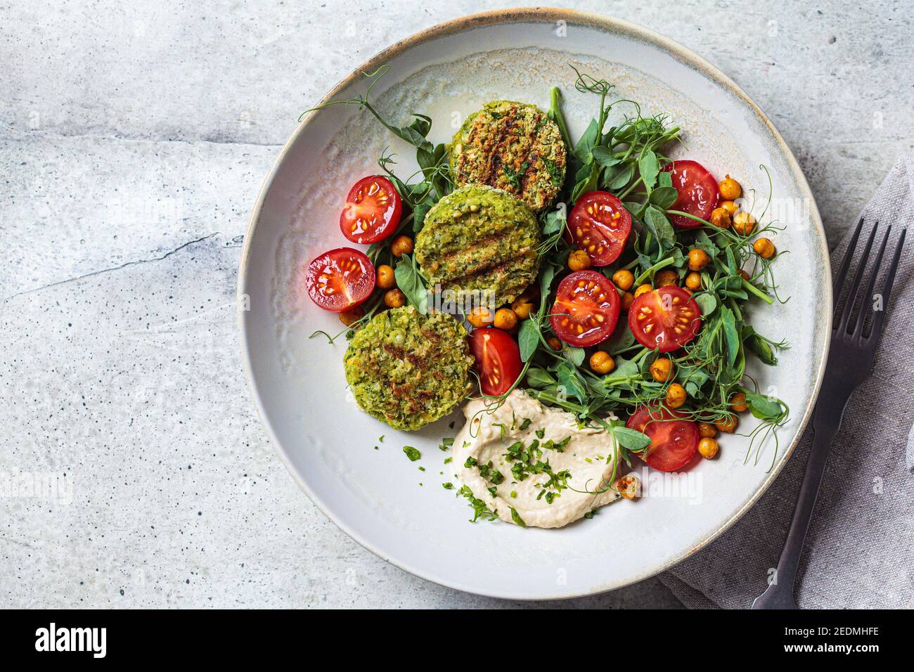 Falafel-Salat mit Tomaten, Hummus und Erbsensprossen in einer grauen Schüssel. Pflanzliches Lebensmittelkonzept. Stockfoto