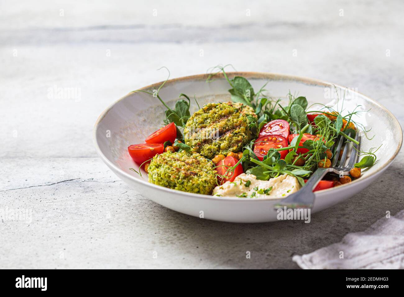 Falafel-Salat mit Tomaten, Hummus und Erbsensprossen in einer grauen Schüssel. Pflanzliches Lebensmittelkonzept. Stockfoto