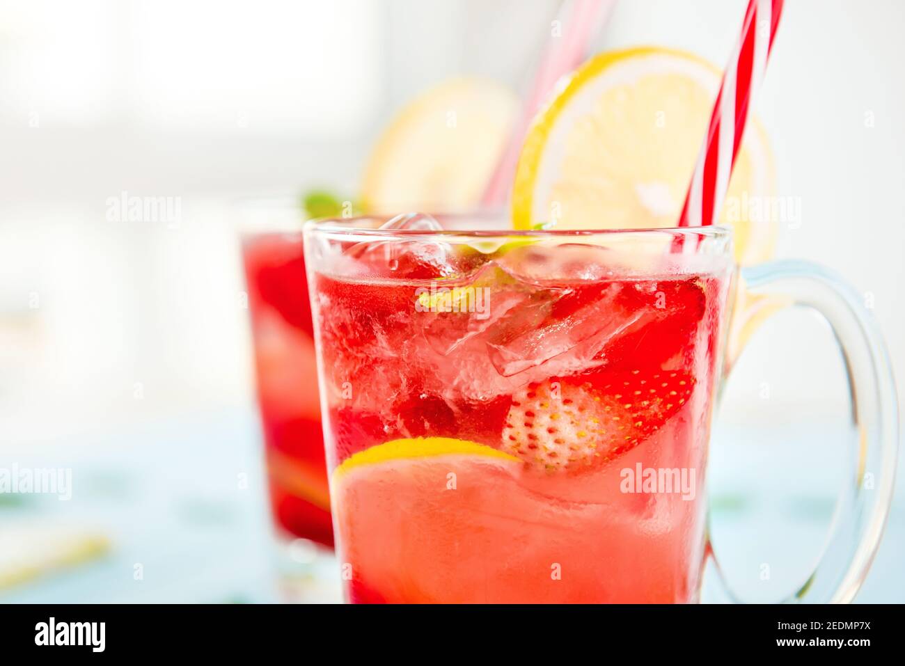 Bunte Erfrischungsgetränke für den Sommer, kalter Erdbeer-Limonensaft mit Eiswürfeln in den Gläsern garniert mit frisch geschnittenen Zitronen Stockfoto