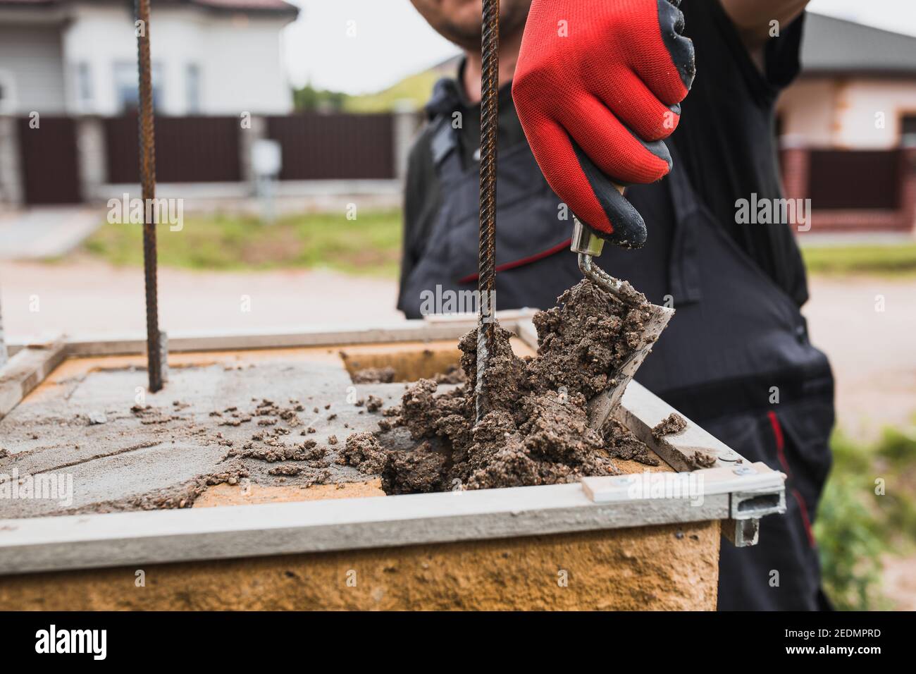 Ein Maurerbauer trägt eine Klebstofflösung auf, um eine zu legen Reihe von Ziegeln und Blöcken an einer Wand Stockfoto
