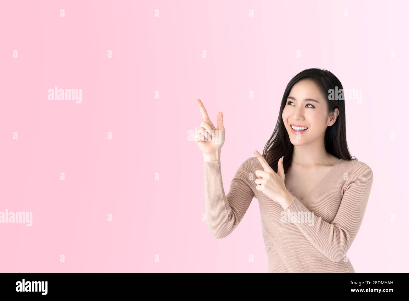 Schöne junge beiläufige asiatische Frau lächelnd und zeigt Hände zu leeren Raum beiseite, Studio auf rosa Hintergrund erschossen Stockfoto