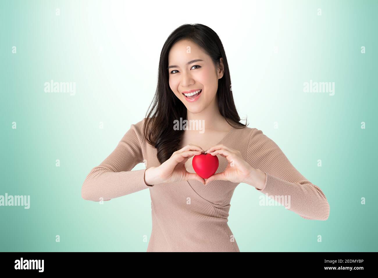 Schöne gesunde lächelnde junge asiatische Frau hält das Herz Form Ball auf türkisgrünen Hintergrund, Studio erschossen Stockfoto