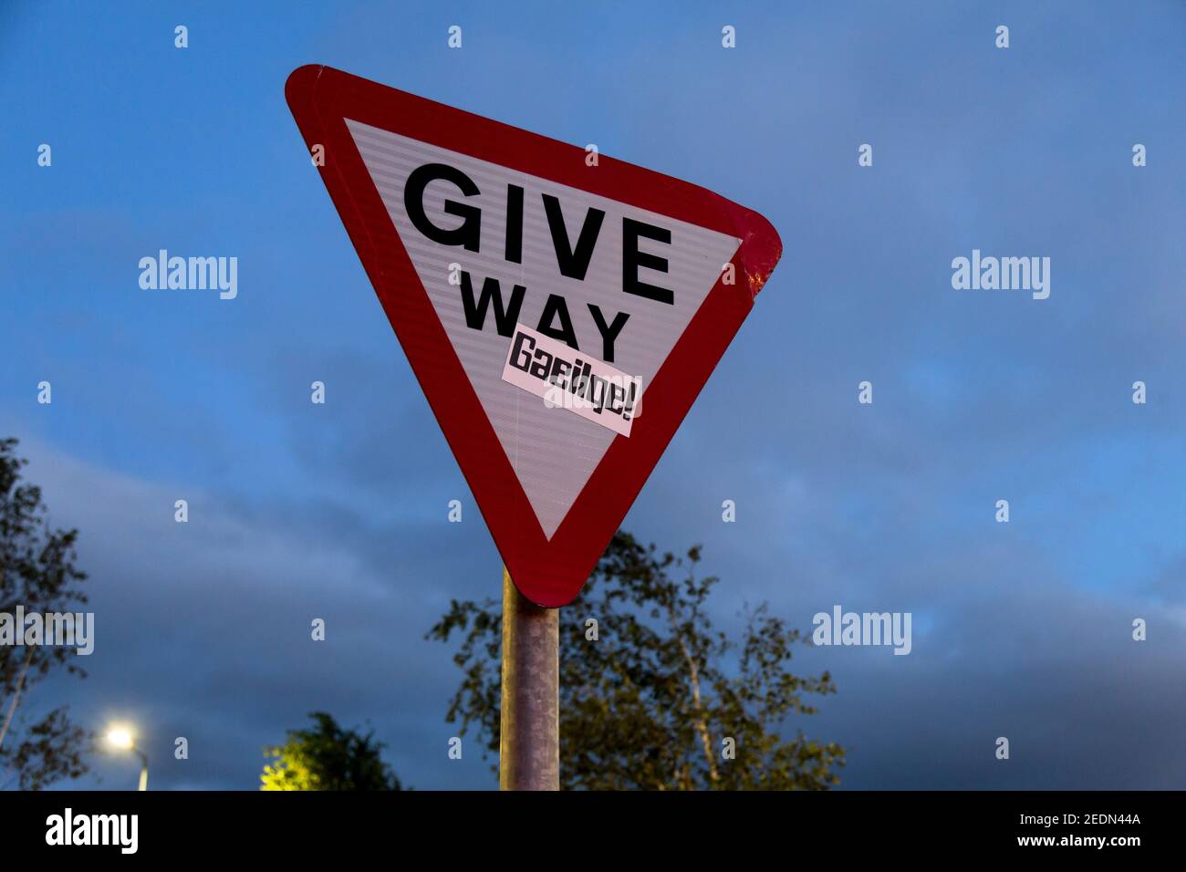 13,07.2019, Belfast, Nordirland, Vereinigtes Königreich - Give Way Schild mit Aufkleber zur Förderung der Verwendung der gälischen Sprache.. 00A190713D258CAROEX.JPG Stockfoto