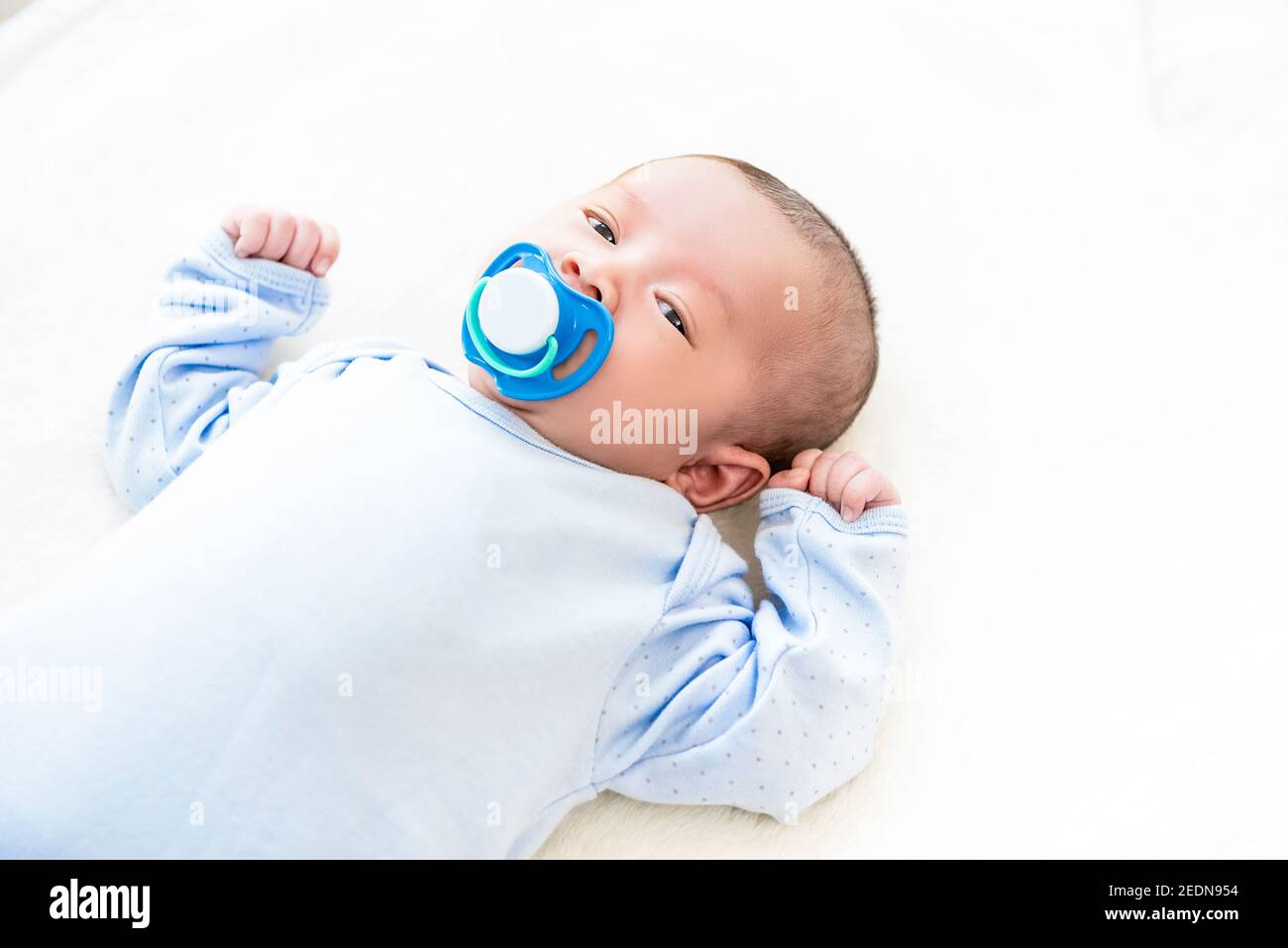 Liebenswert kleines neugeborenes Baby liegt auf weißem Bettlaken mit Dummy in ihrem Mund Stockfoto