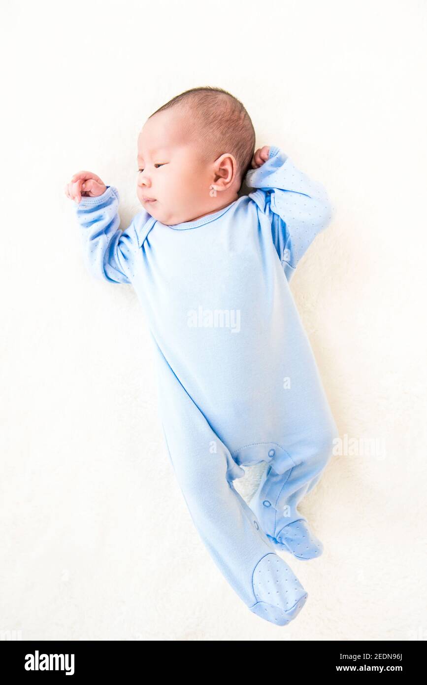 Neugeborenes hübsches Baby in der Schlafkleidung liegend auf weißem Laken, Ansicht von oben Stockfoto