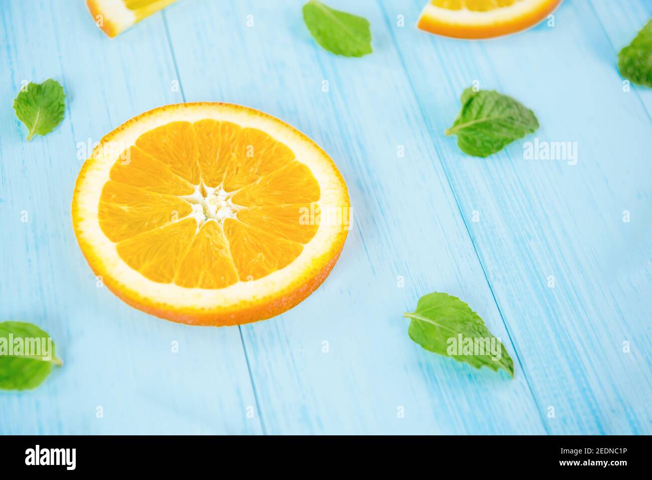 Frisches Obst für den Sommer, saftig geschnittene Orangen mit Pfefferblättern auf hellblauem, pastellfarbenem Holzhintergrund Stockfoto