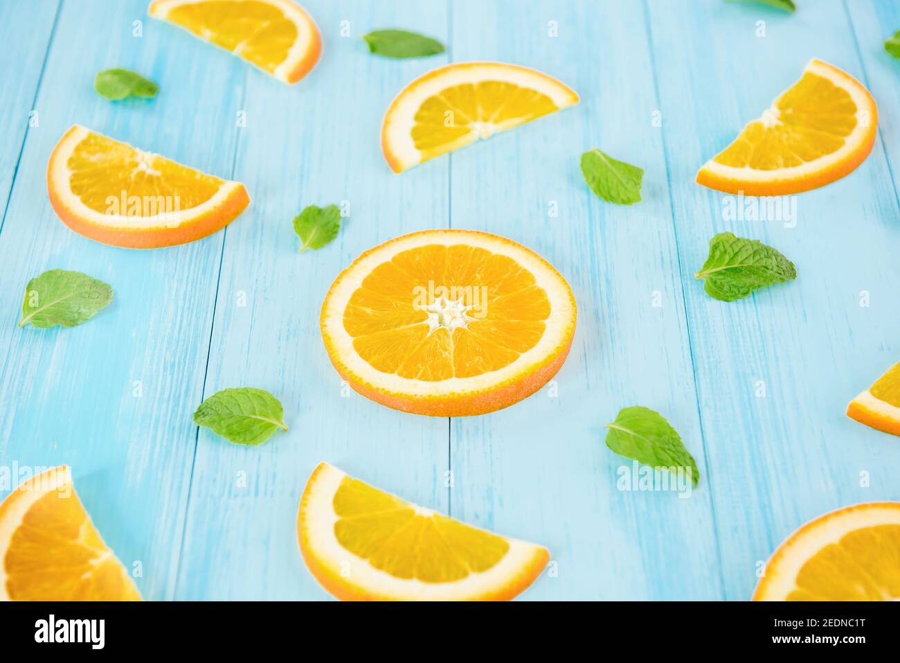 Frisches Obst für den Sommer, saftig geschnittene Orangen mit Pfefferblättern auf hellblauem, pastellfarbenem Holzhintergrund Stockfoto