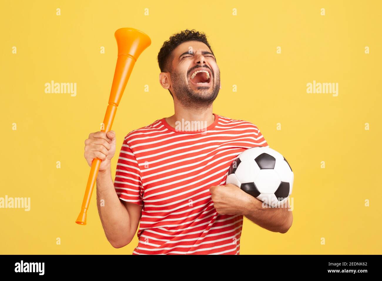 Extrem glücklicher bärtiger Mann in rot gestreiftem T-Shirt mit Horn und  schwarz-weißem Fußball, der den Sieg der Lieblings-Fußballmannschaft  feiert. Indoo Stockfotografie - Alamy