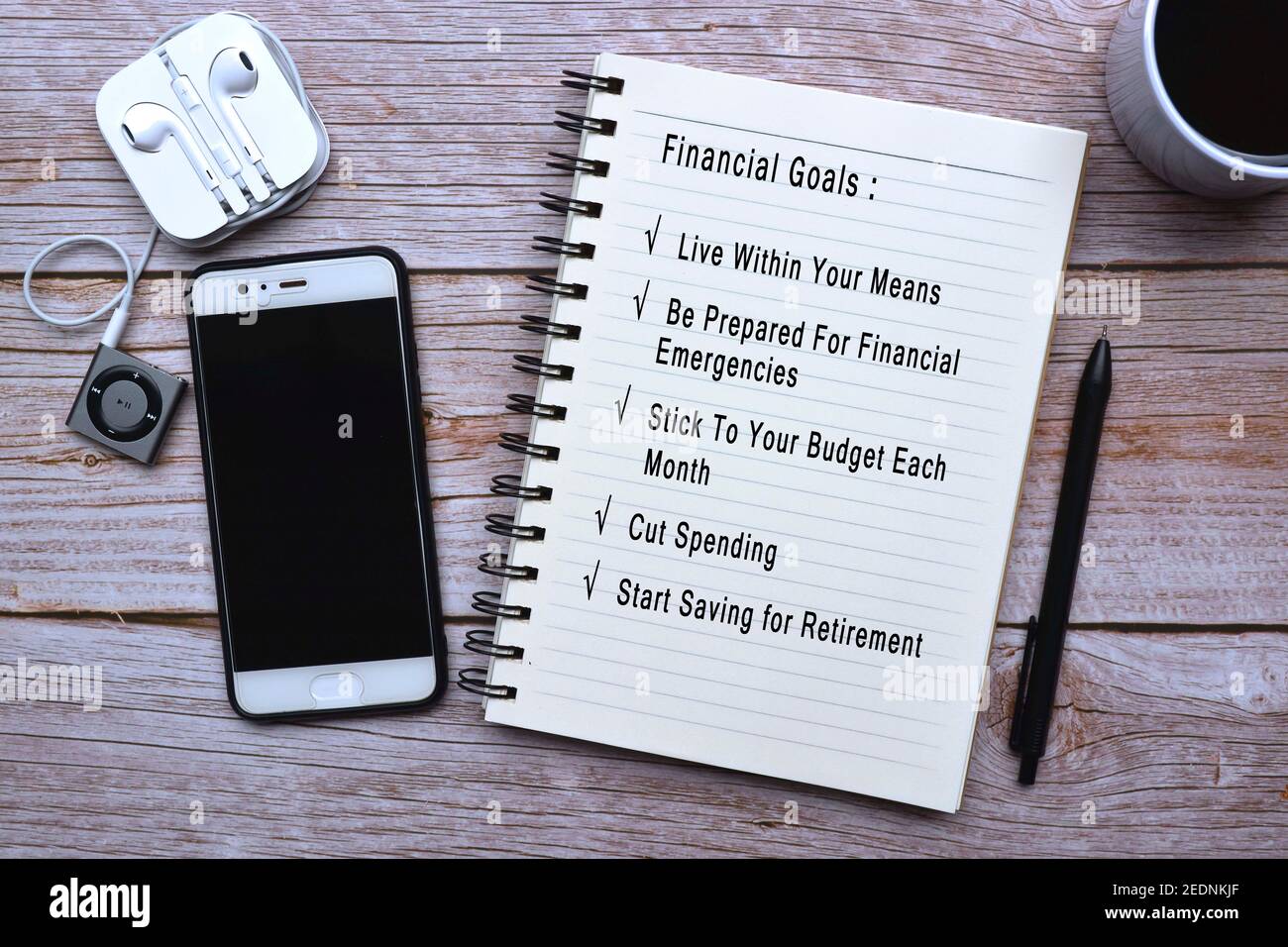 Text auf Notizblock mit Tasse Kaffee, Smartphone, Musik-Player und Stift auf Holzschreibtisch - finanzielle Ziele Liste Stockfoto
