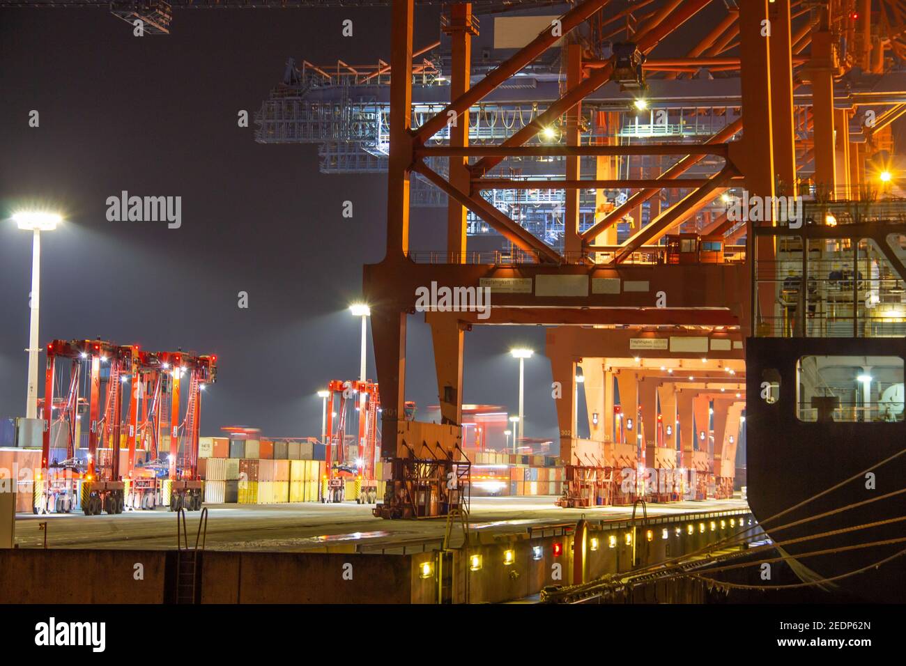 Pier des Containerhafens während des Verladevorgangs mit Kräne, Schiff und Container in der Nacht mit Licht Stockfoto