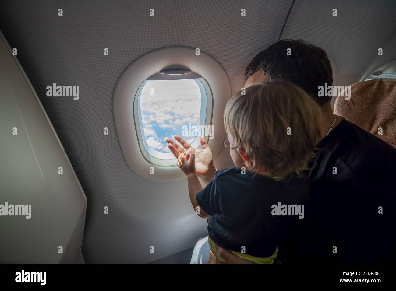 Vater und niedliche Kleinkind sitzen auf einem Flugzeug und Blick in den Himmel durch das Bullauge. First Flight Konzept, Reisen mit Kindern. Stockfoto