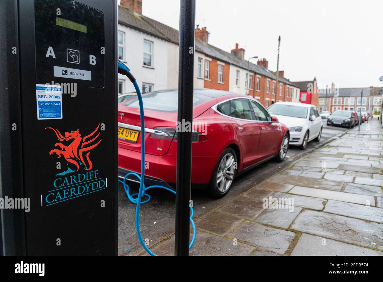 Cardiff, Wales, UK - Februar 14th 2021: Ein rotes Tesla-Elektroauto (EV) nutzt eine Ladestation, die von Cardiff Council bereitgestellt wird, in einer Wohnstraße. Stockfoto