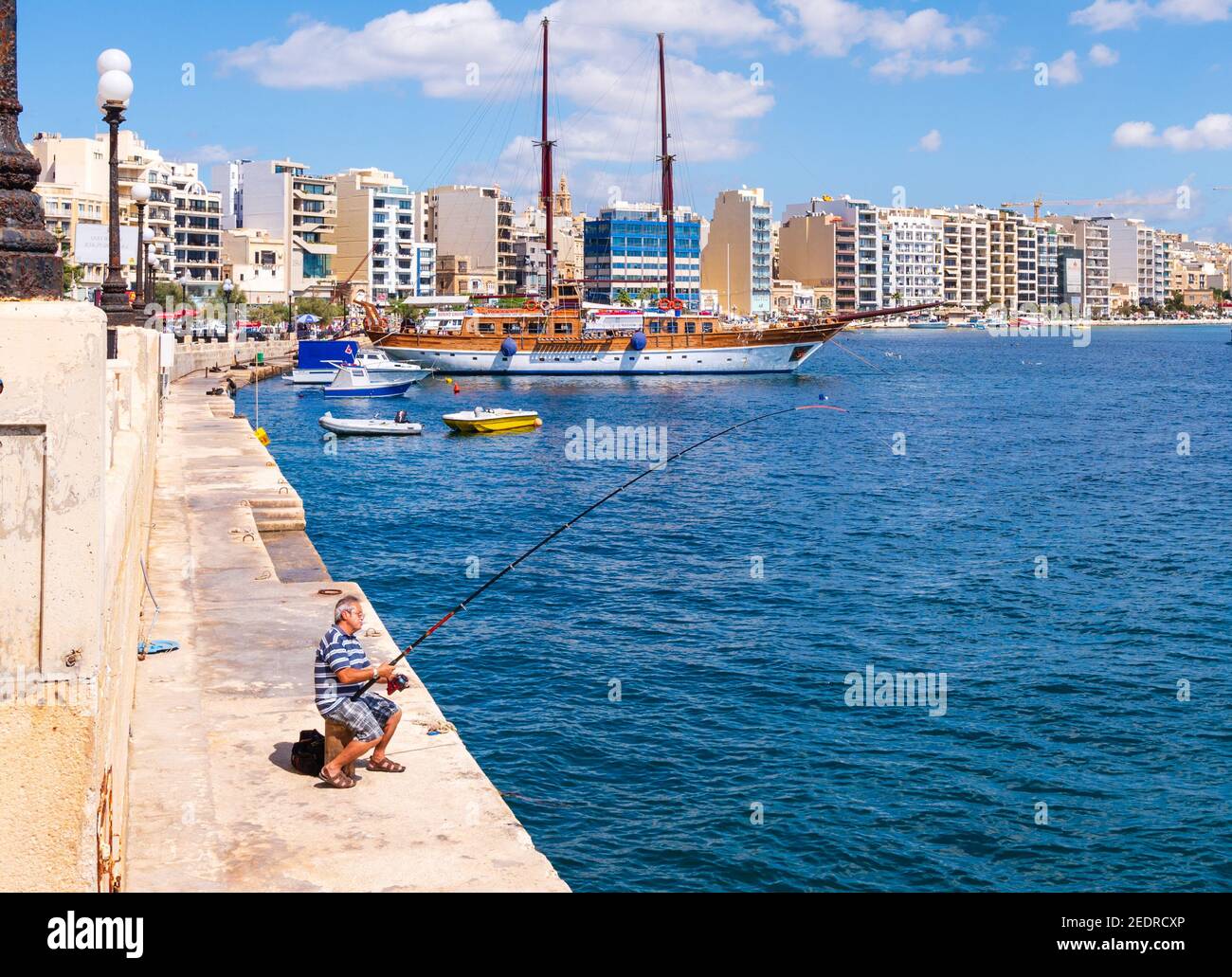 Alter Mann, der auf den nahe gelegenen modernen Apartments und Hotels angeln kann An der Tigné Seafront Sliema Malta Stockfoto