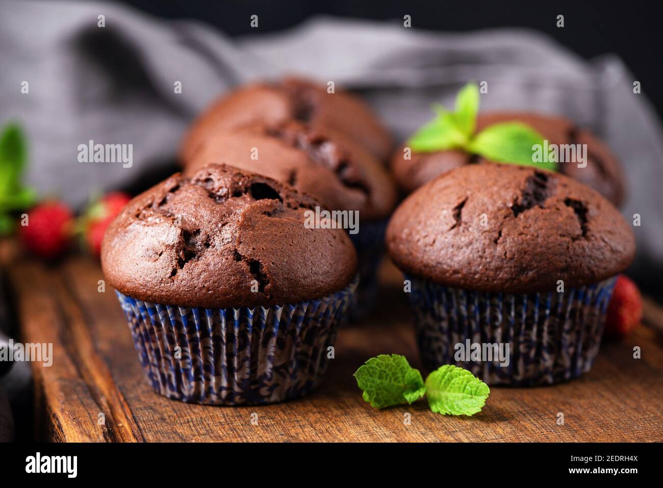 Schokoladenmuffins in violetten Pappbechern auf Holzbrett, Nahaufnahme. Leckere Schokoladen-Cupcakes ohne Sahne Stockfoto