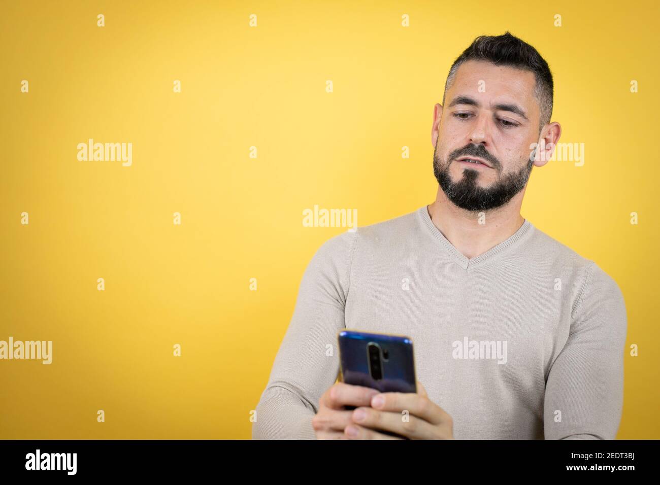 Schöner Mann mit Bart trägt Pullover über gelben Hintergrund Texting Mit ihrem Telefon Stockfoto