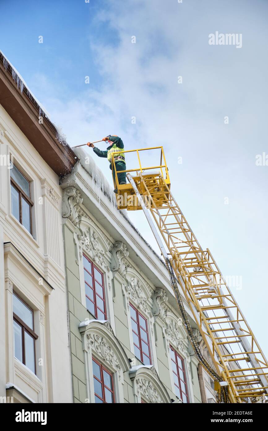 Öffentliche Versorgungseinrichtungen auf Spezialfahrzeugen entfernen Eiszapfen von den Dächern der Häuser auf dem Rynok-Platz in Lviv. Dacharbeiter Im Winter. Stockfoto