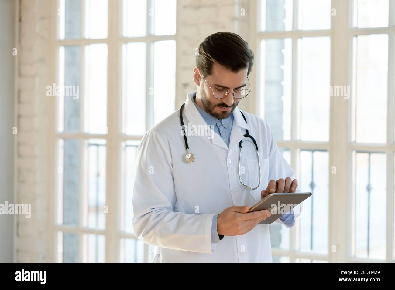 Fokussierte junge männliche Arzt mit elektronischen digitalen Touchscreen-Gadget. Stockfoto