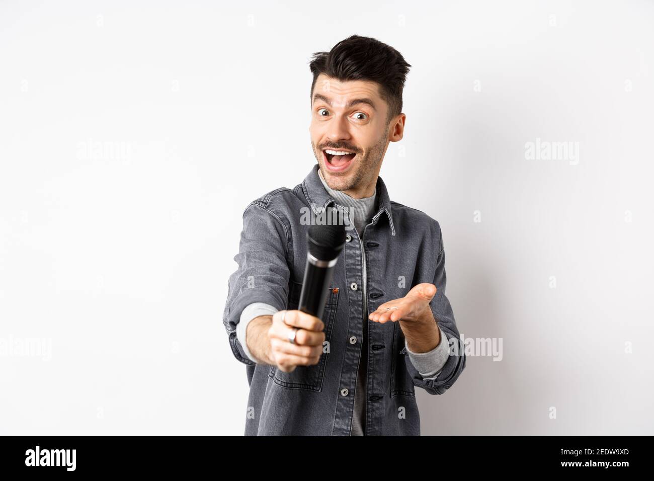 Schöner lächelnder Mann Strecke die Hand mit Mikrofon aus und gibt dir das  Mikrofon, stehend auf weißem Hintergrund Stockfotografie - Alamy