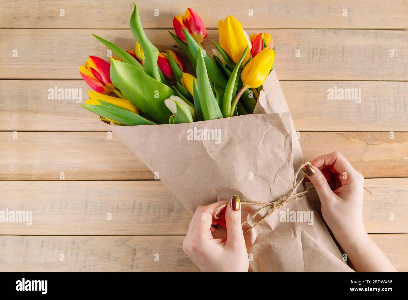 Der Prozess der Verpackung Bouquet von frischen Tulpen in umweltfreundliche Handwerk Papier. Schritt 3. Geschenk für Frühlingsferien. Blumengeschäft. Stockfoto