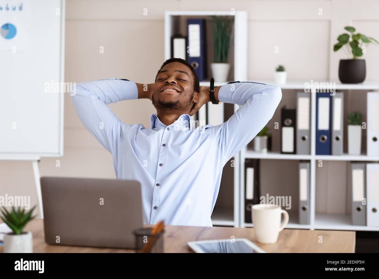 Fröhlicher afroamerikanischer Angestellter, der sich auf seinem Stuhl ausruhte Stockfoto
