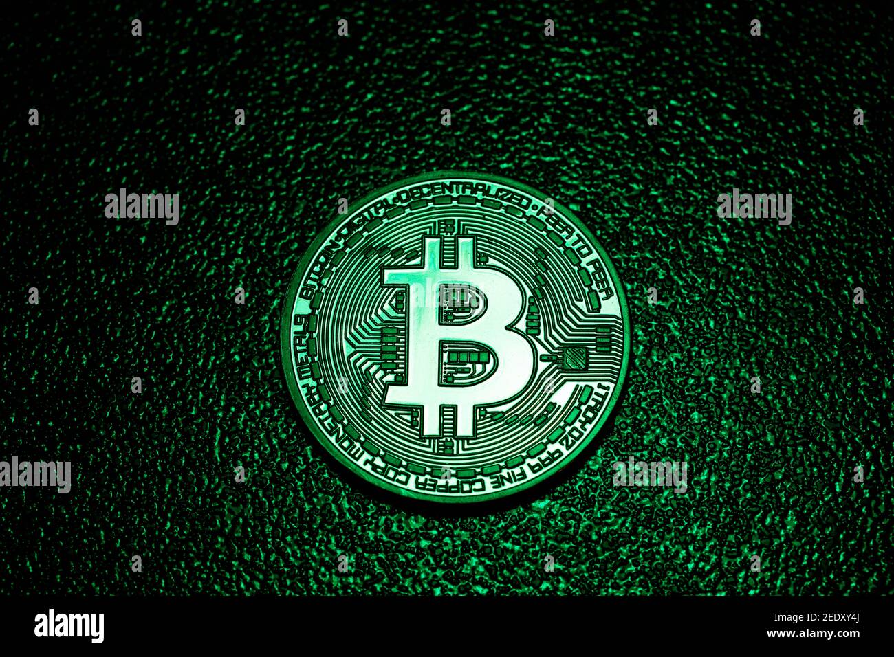 Eine Münze mit Bitcoin-Logo in grüner Beleuchtung. E-Business. Kryptowährung und Kryptographie. Stockfoto