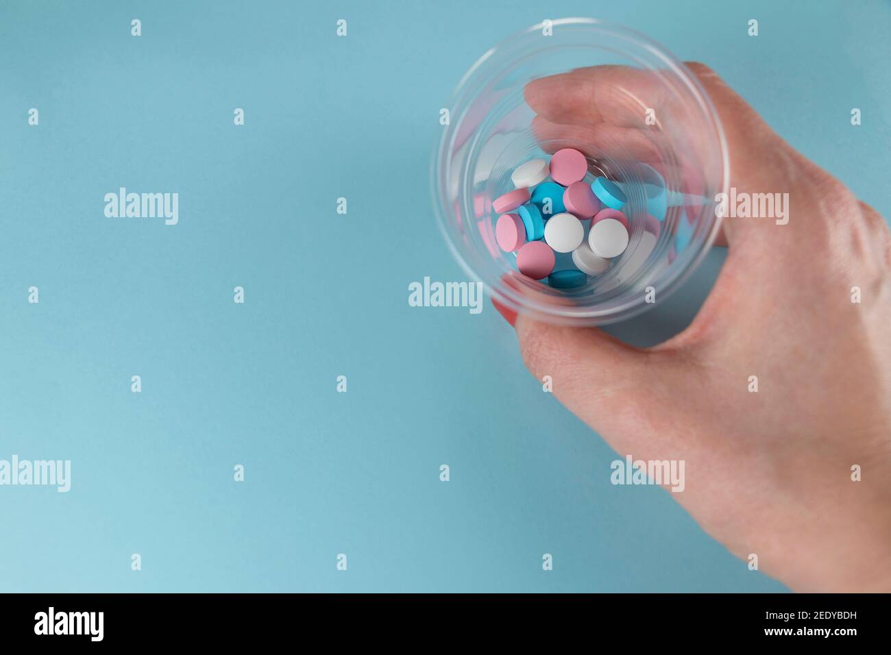 Medizin und Pillen. Weibliche Hand hält Pillen in einem kleinen Plastikbecher Medizin.Multi-farbige Medikamente auf pastellblauem Hintergrund. Stockfoto