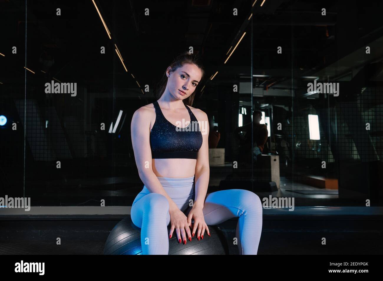 Fit Frau sitzt auf einem Ball mit Fitnessgeräten im Fitnessstudio, Trainer eine Pause, um sich während des Trainings abzukühlen Stockfoto