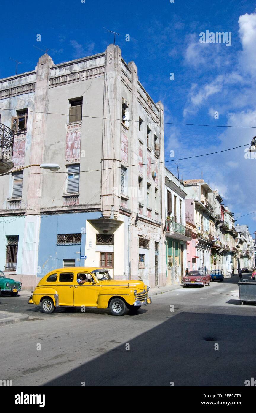Ein gelbes Auto, das als Service-Taxi fungiert, das eine Straße im Zentrum von Havanna, Kuba, hinunterfährt. Stockfoto