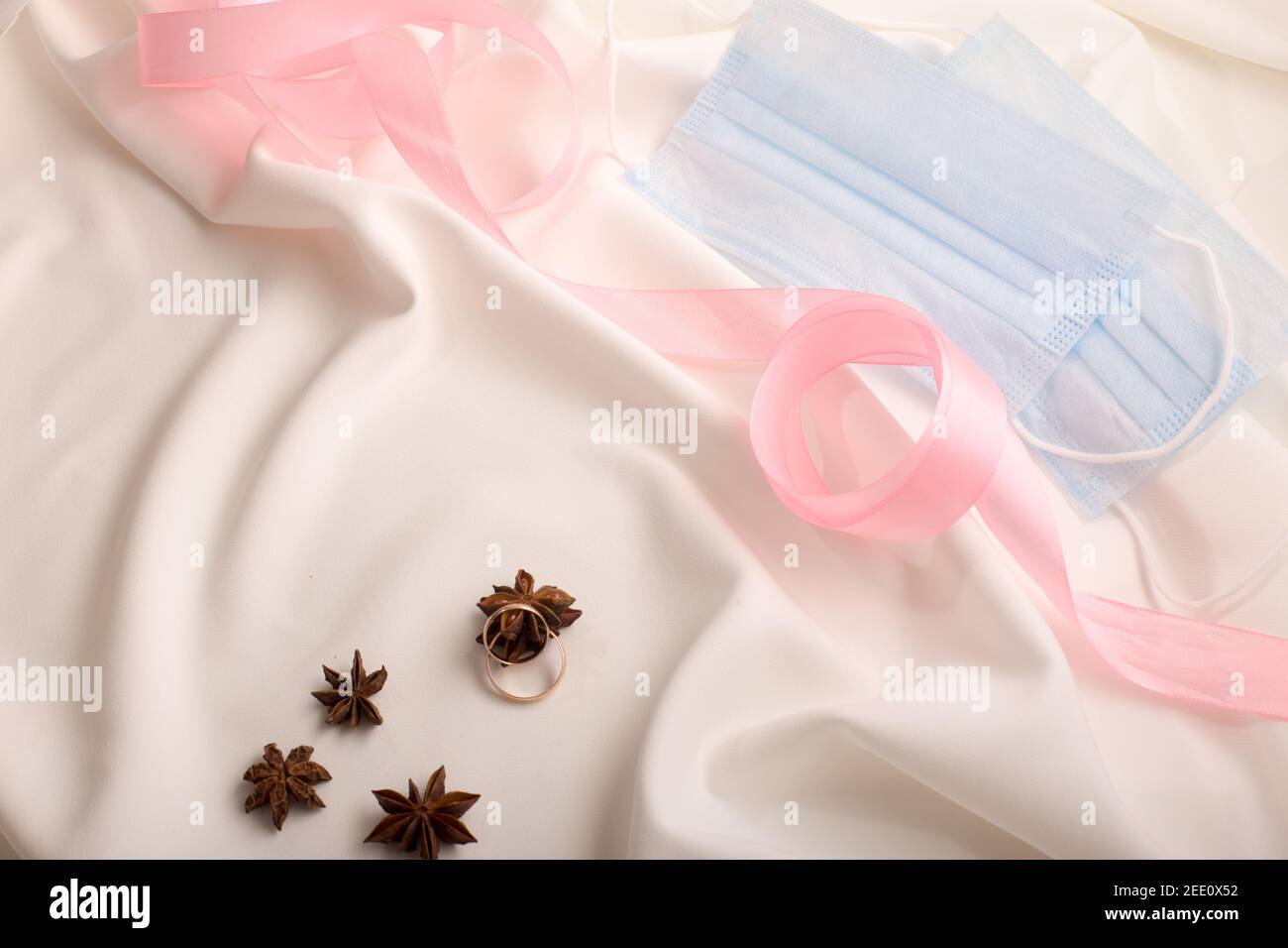 Eheringe auf einem weißen Kleid mit rosa Klebeband und Sternanis Stockfoto