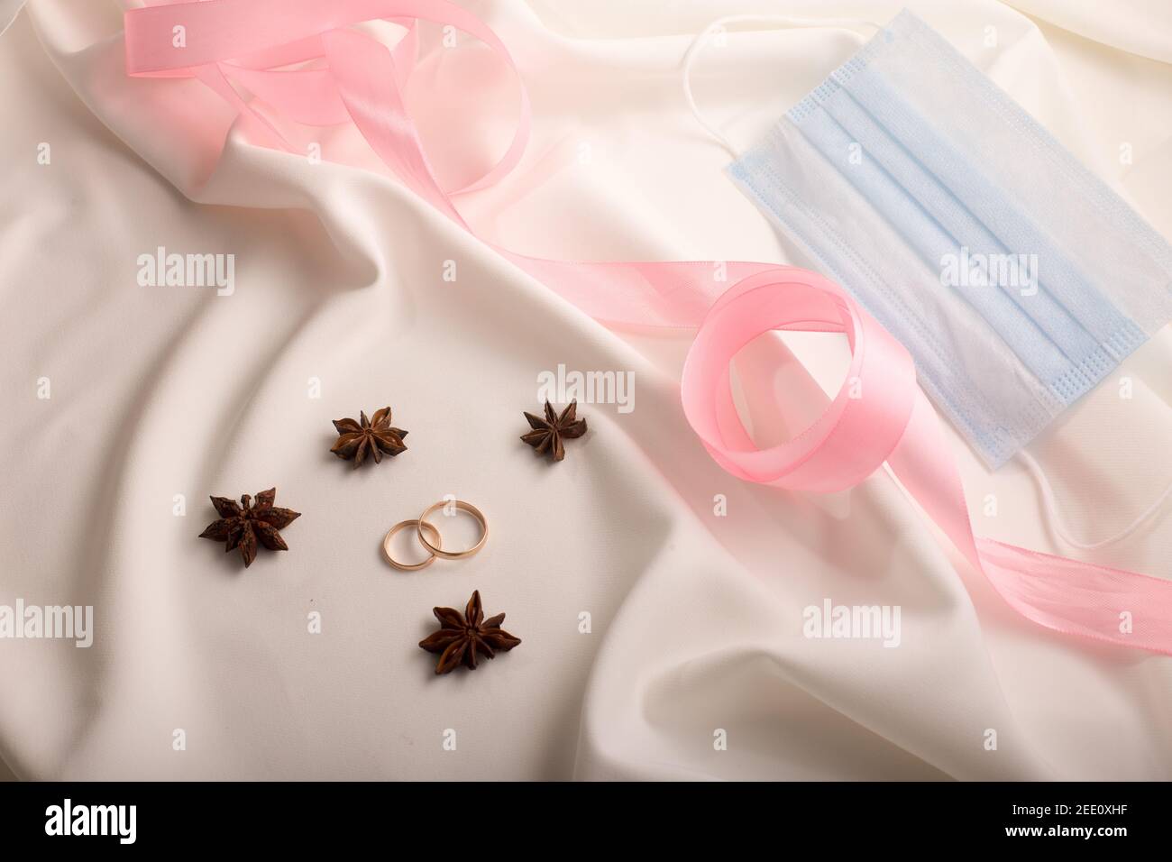 Eheringe auf einem weißen Kleid mit rosa Klebeband und Sternanis Stockfoto